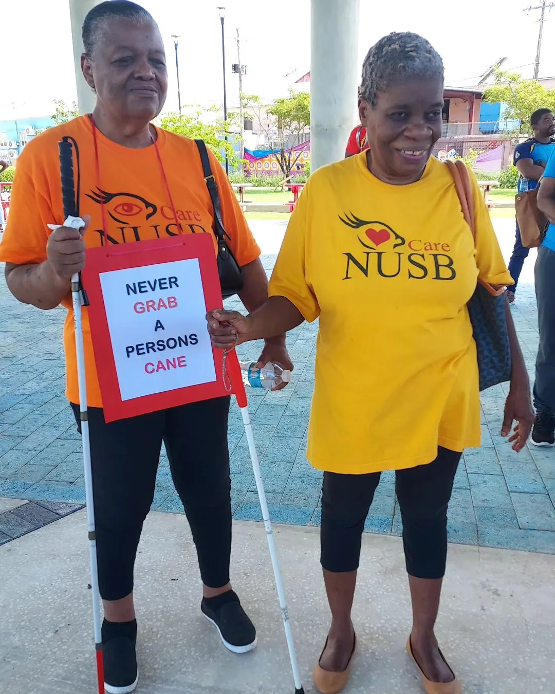Two women at a white cane awareness event, one carrying a cane